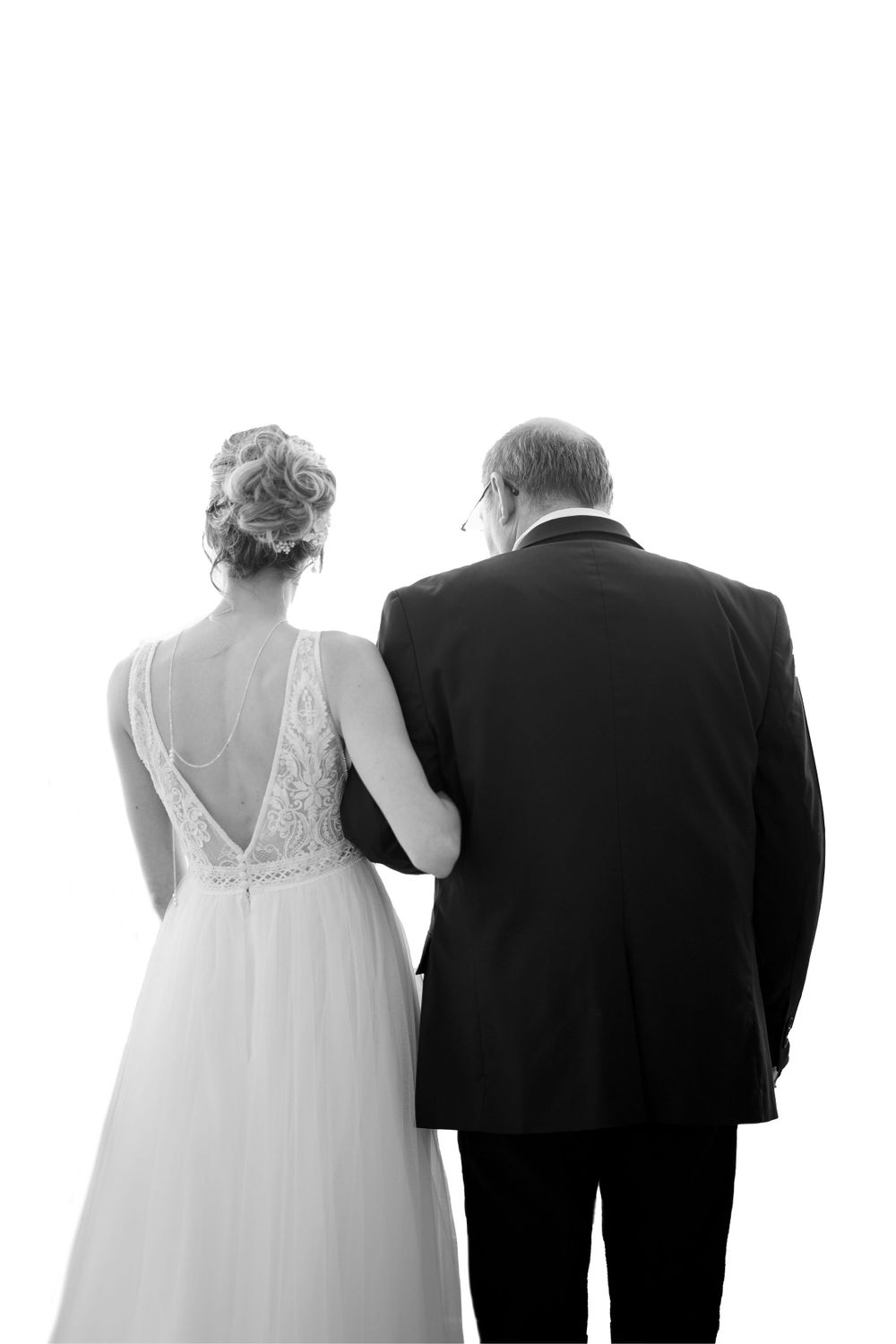 Black and white photograph showing back view of a couple in formal wedding attire.