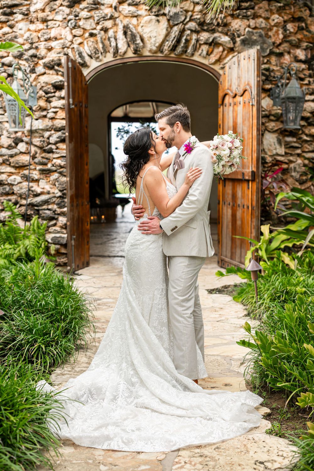 Romantic moment captured in a stone archway with lush garden surroundings and wrought iron details.