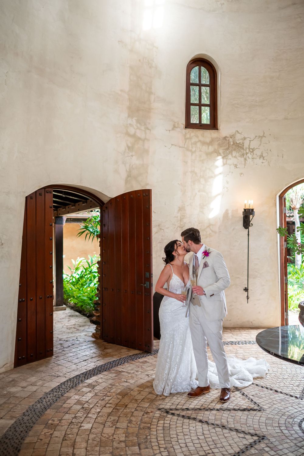 Wedding couple embracing in a Mediterranean-style corridor with arched window and wooden doors.