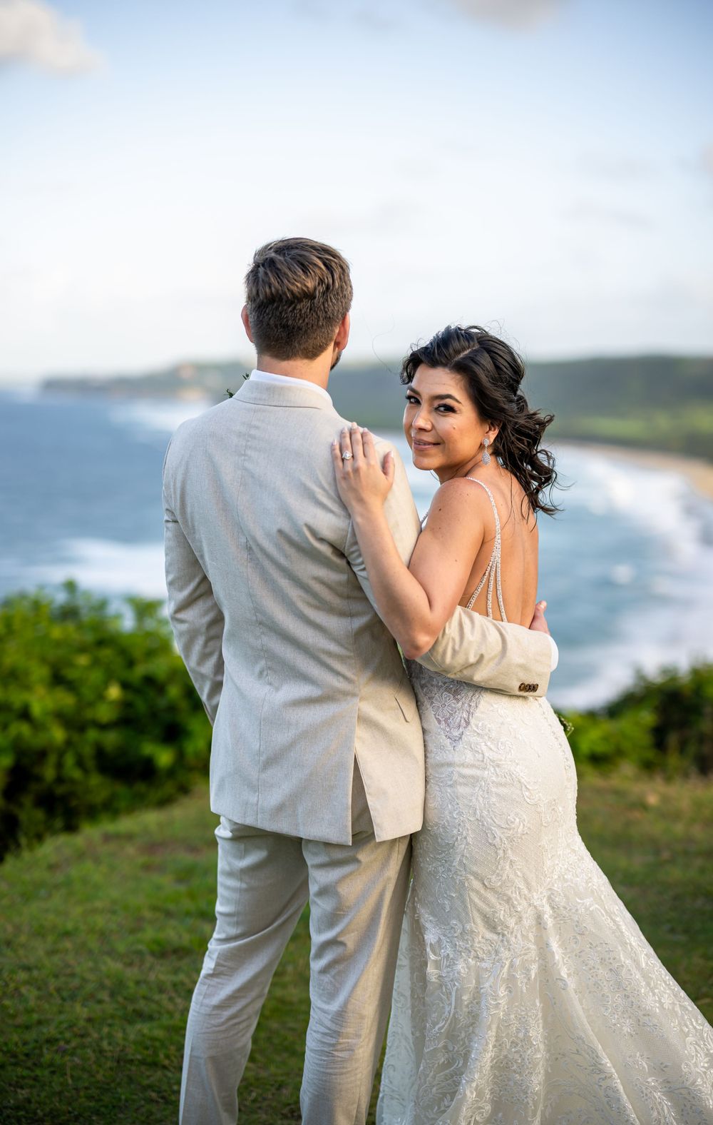 Wedding couple embracing on coastal cliff overlooking ocean waves.