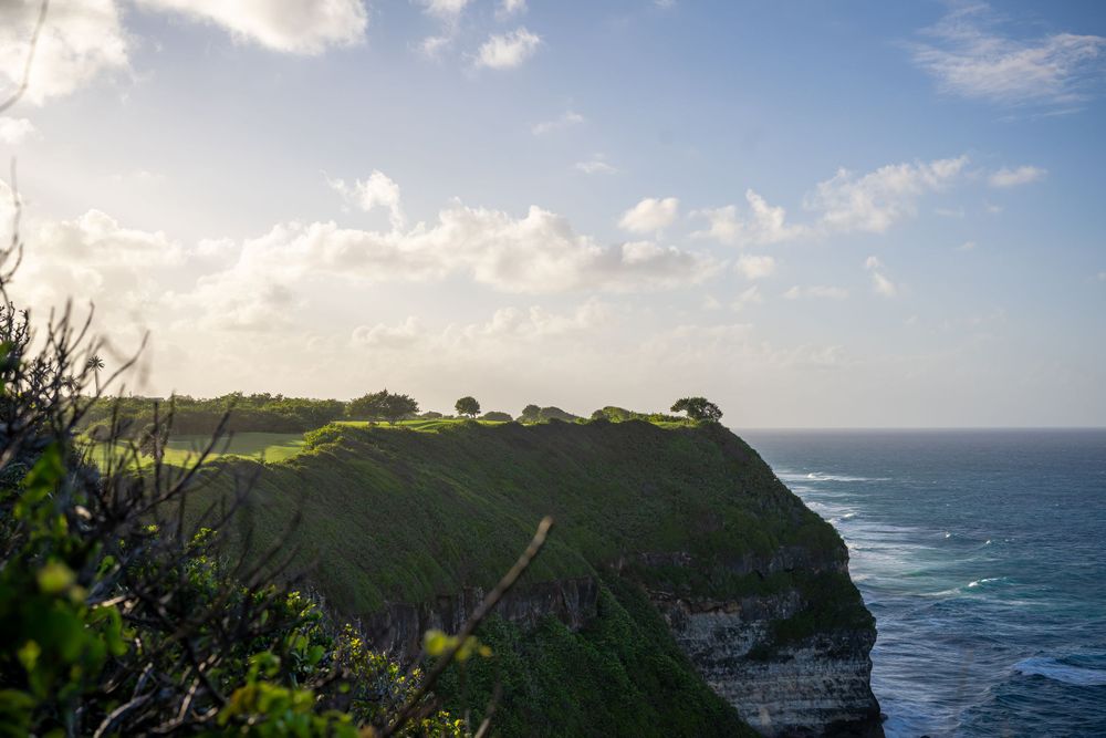 Dramatic coastal cliffs and ocean waves under bright blue sky.