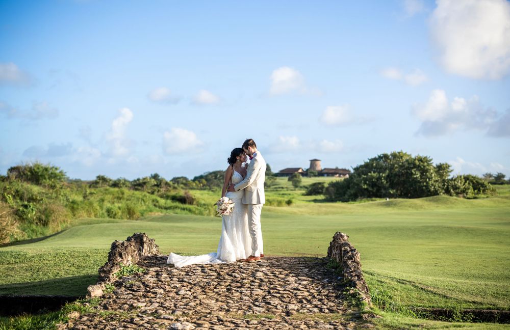 Newlyweds stand together on elevated stone platform overlooking green landscape.