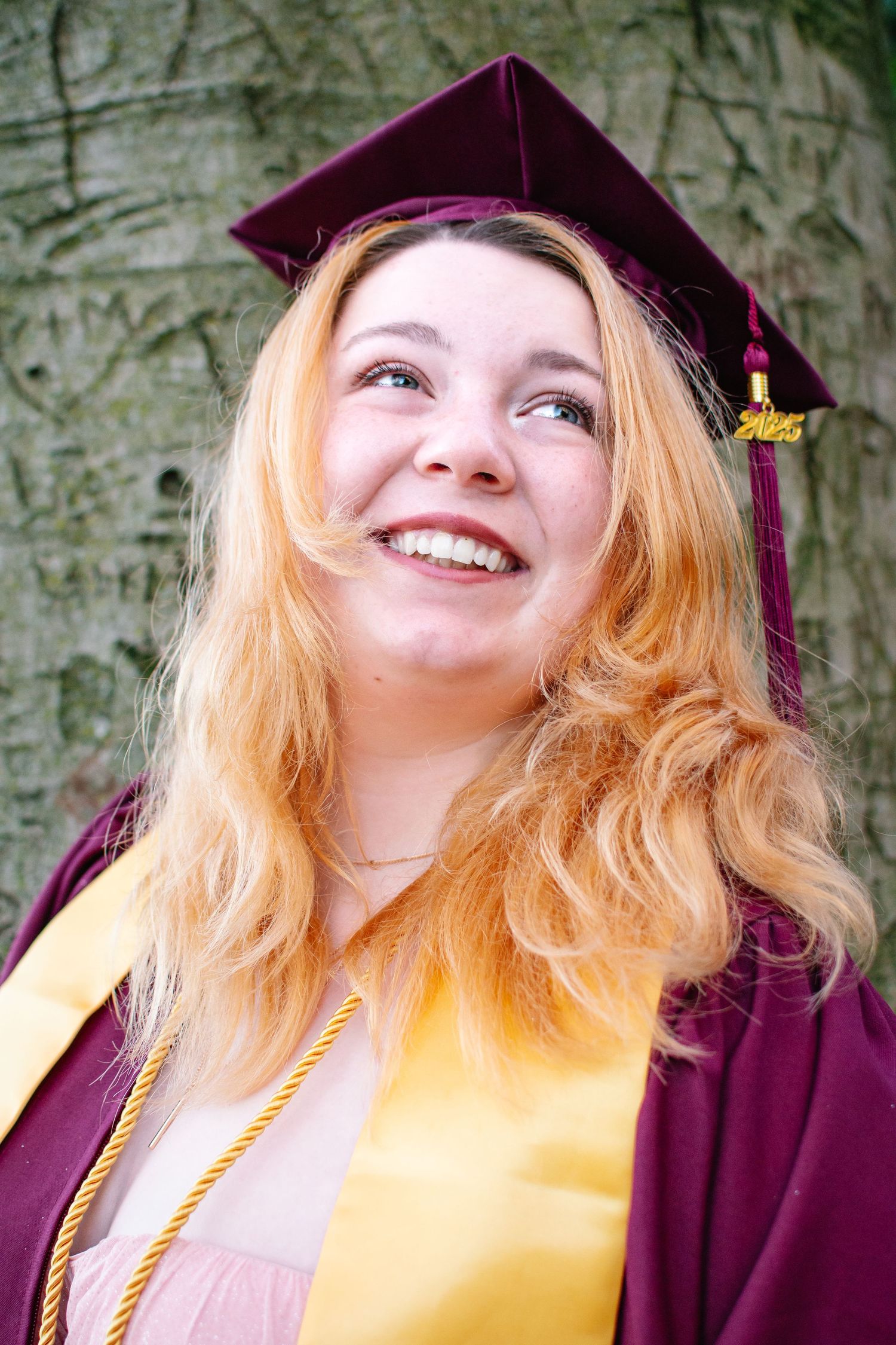 Joyful senior portrait of graduate in maroon cap and gown with golden stole taken at Kerry Park in Seattle