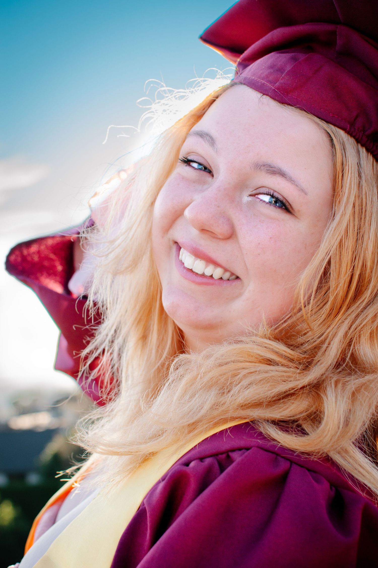 Close-up graduation portrait with senior smiling and tilting maroon cap, Seattle senior photography session.
