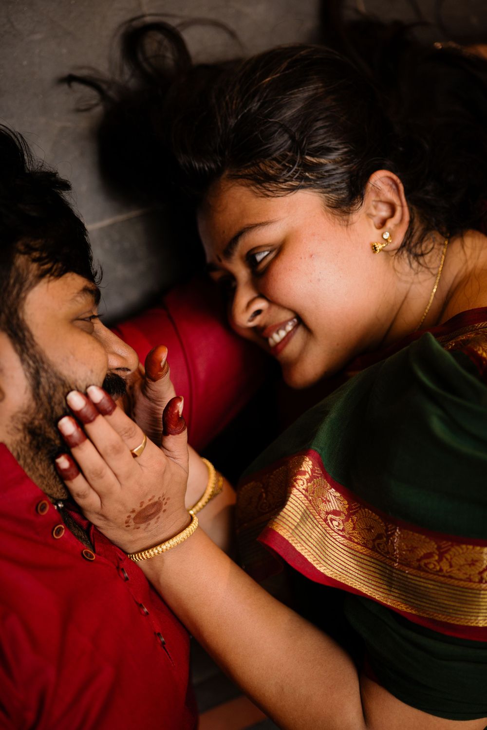 A couple in traditional Indian attire share an intimate moment with bright red and green colors.
