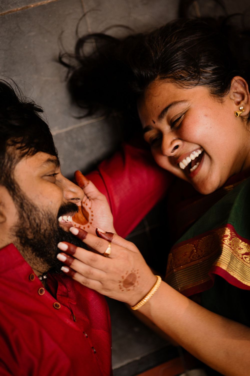 A playful couple lying down and laughing together, wearing traditional Indian attire.
