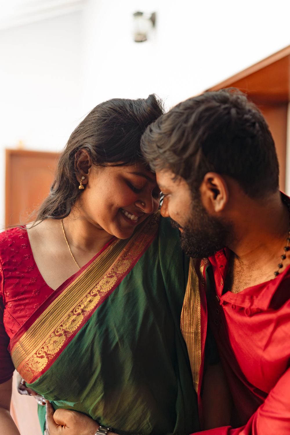 A tender moment between a couple wearing traditional Indian clothing with red and green sari details.