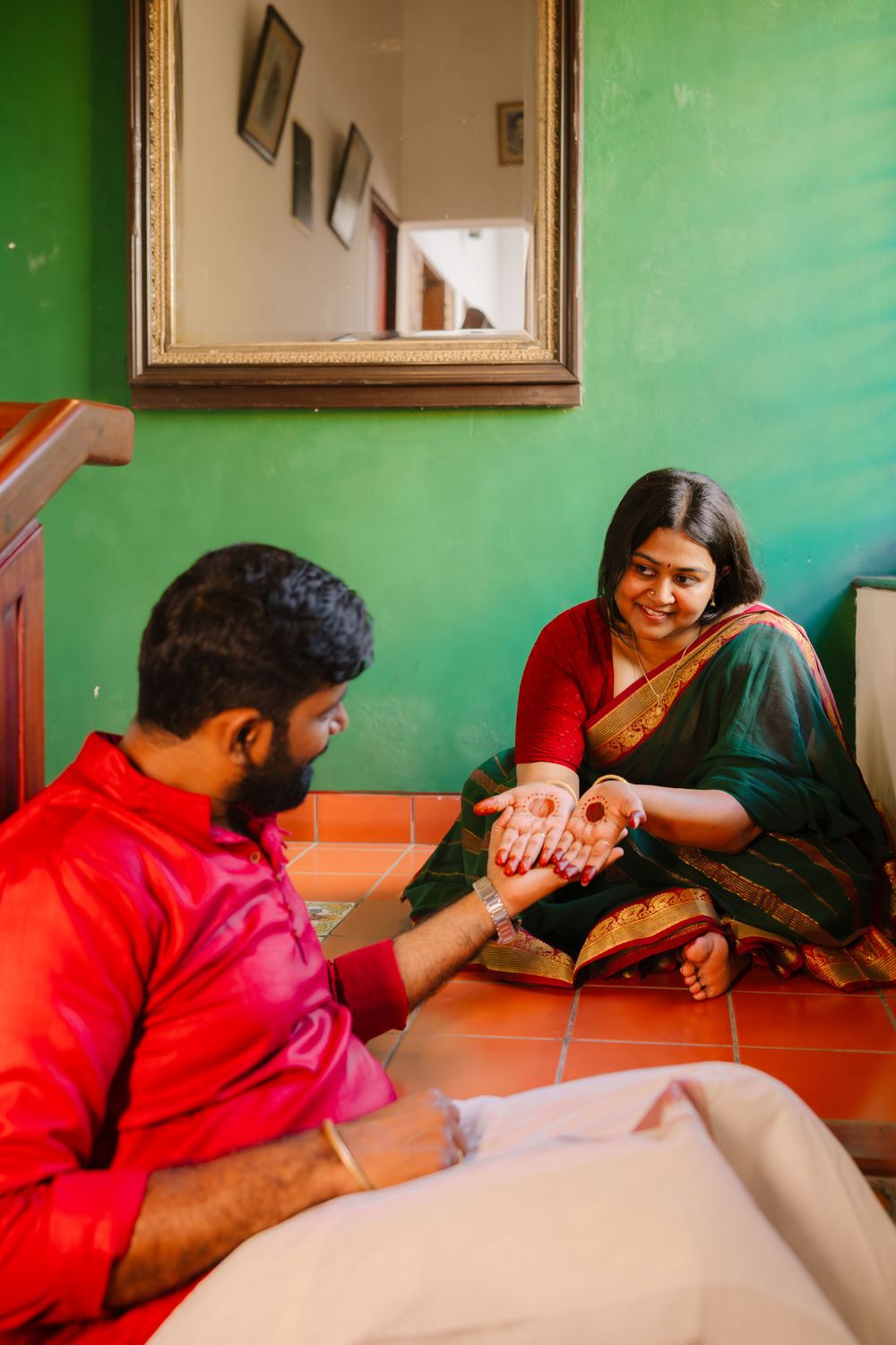 A couple in traditional Indian dress sharing a special moment beside a green wall with a mirror.