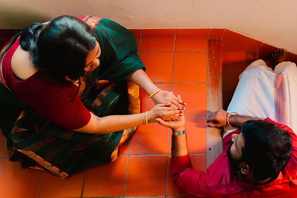 Two figures sitting on an orange floor share a tender moment while holding hands together.