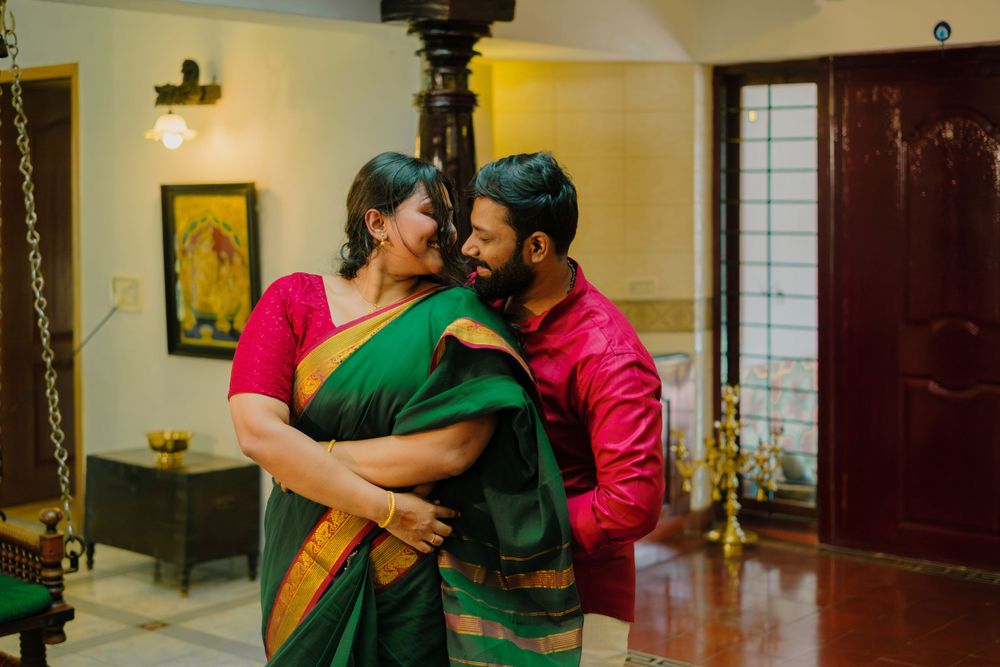 A couple in traditional Indian attire share an intimate moment in a warmly lit room with traditional decor.