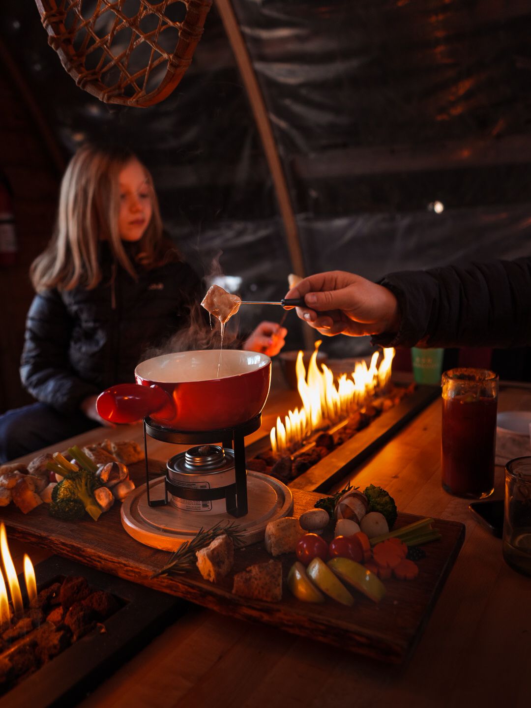 Cozy candlelit table with food and drinks being prepared in a dark, intimate setting.