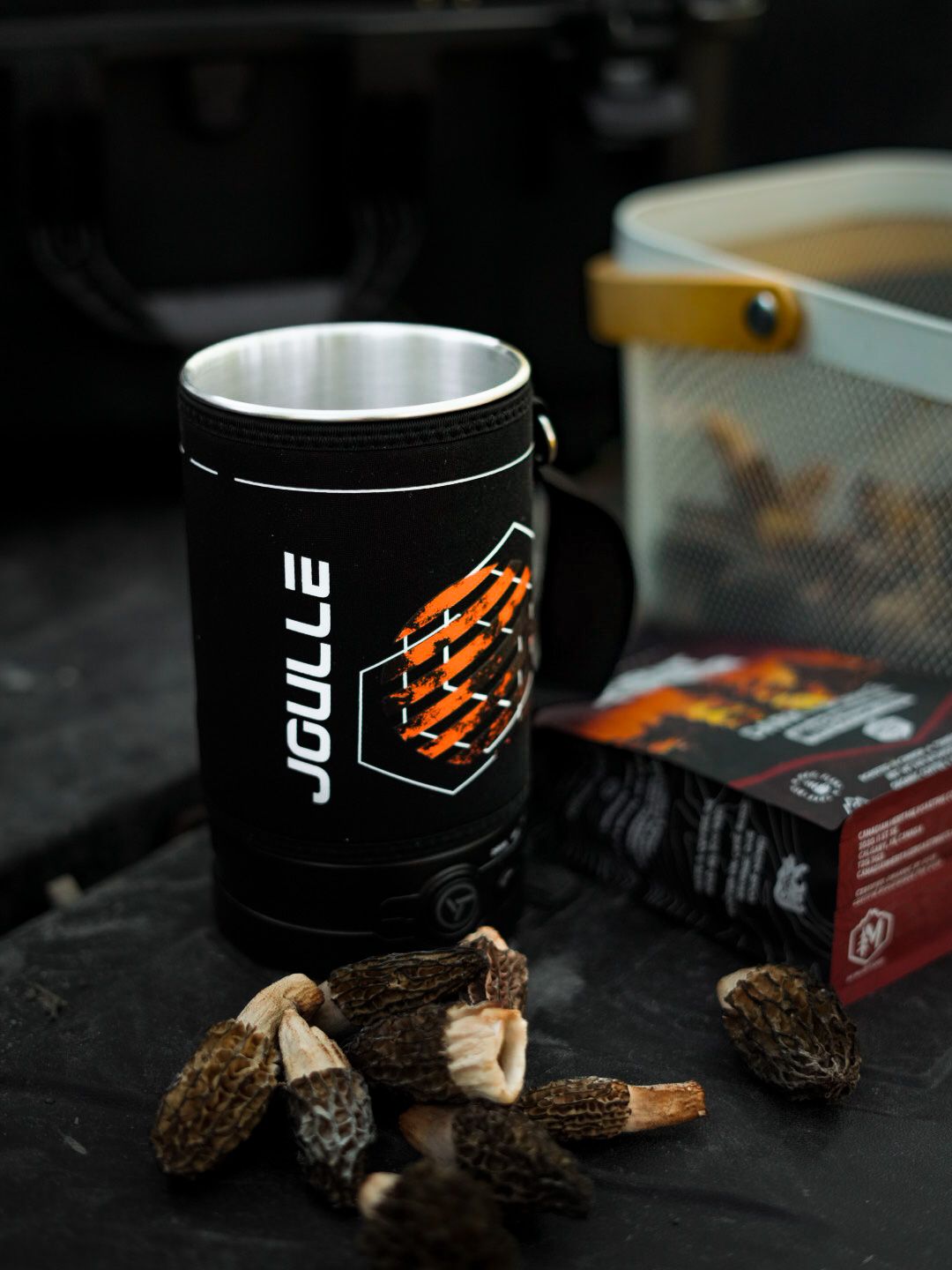 Black branded cups and packaging displayed with wood chunks on dark surface.