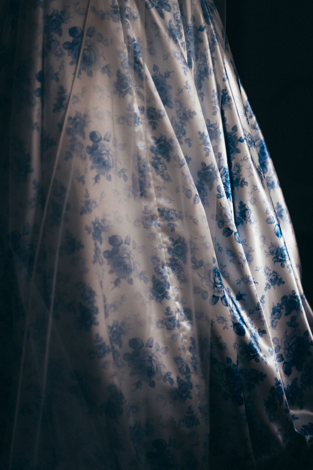 Elegant white fabric with blue floral pattern draped gracefully, showcasing delicate rose prints on flowing textile material.