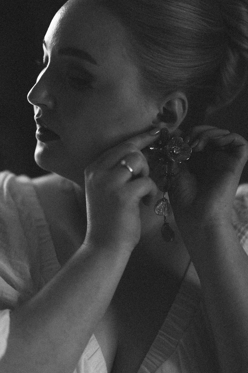 Black and white portrait of woman adjusting ornate earring, showing elegant profile and shoulder in artistic lighting.
