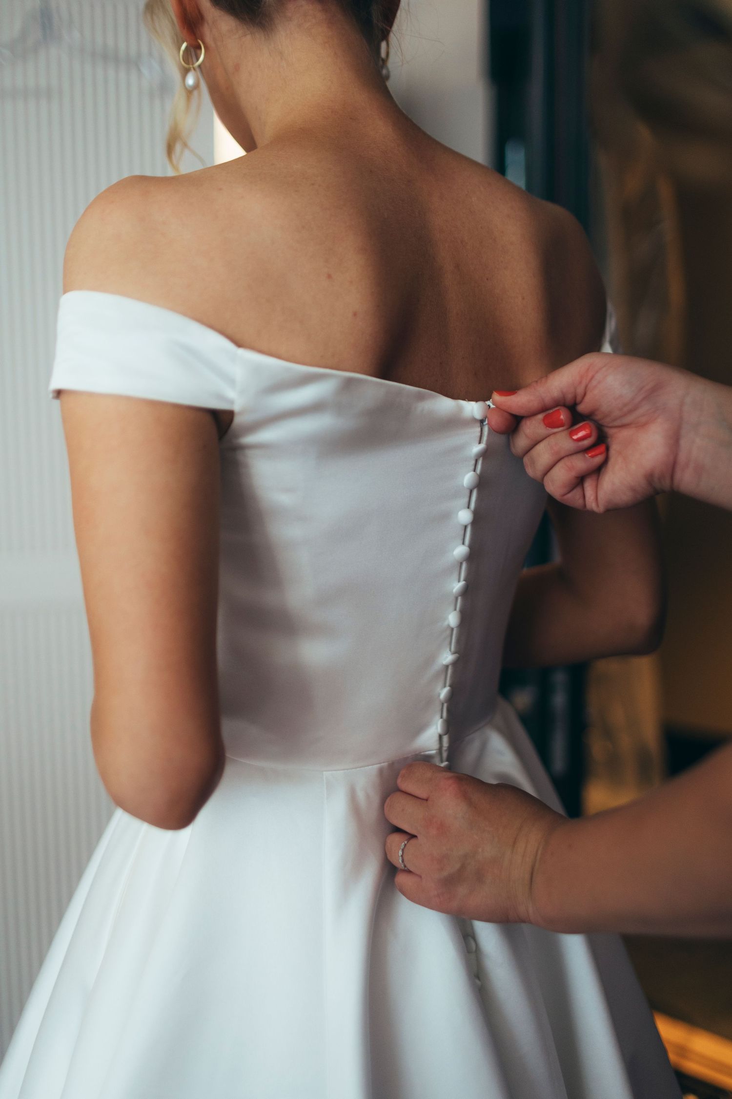 Close-up details of white wedding dress buttons being fastened.