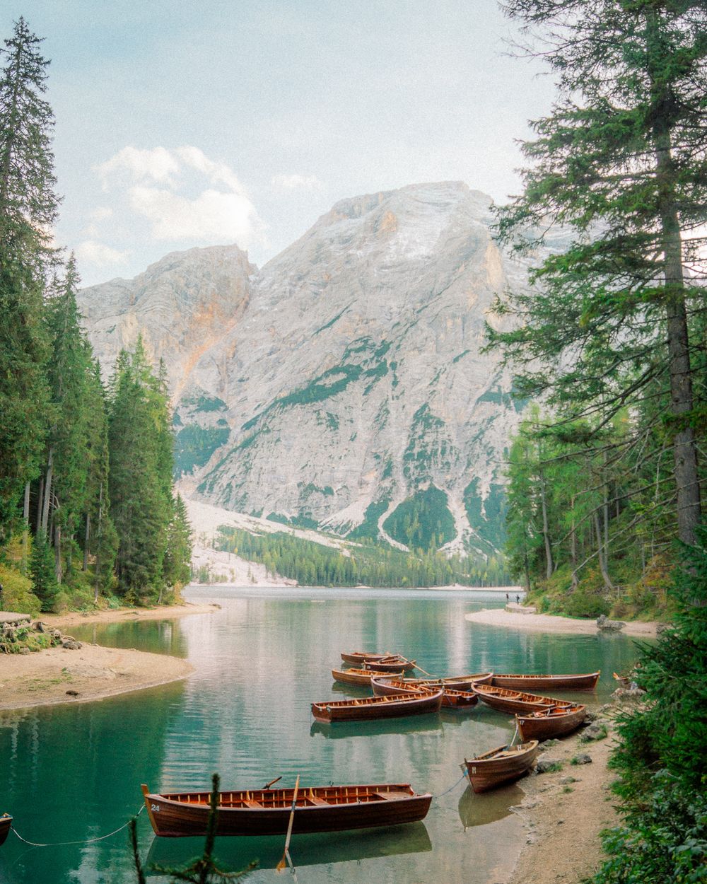 Alpine lake with wooden boats and pine forest reflecting in calm waters
