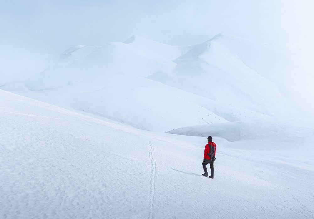 Lone figure crossing a snowy plateau under overcast sky