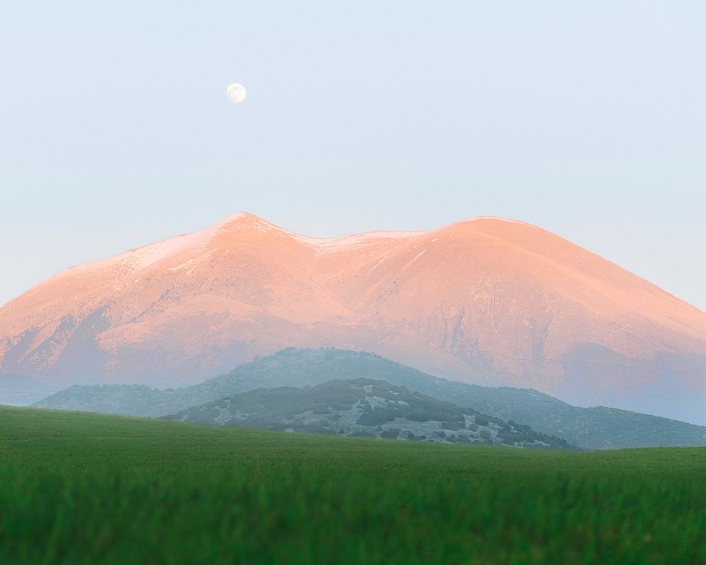 Golden mountaintop emerging from clouds over a sunlit meadow
