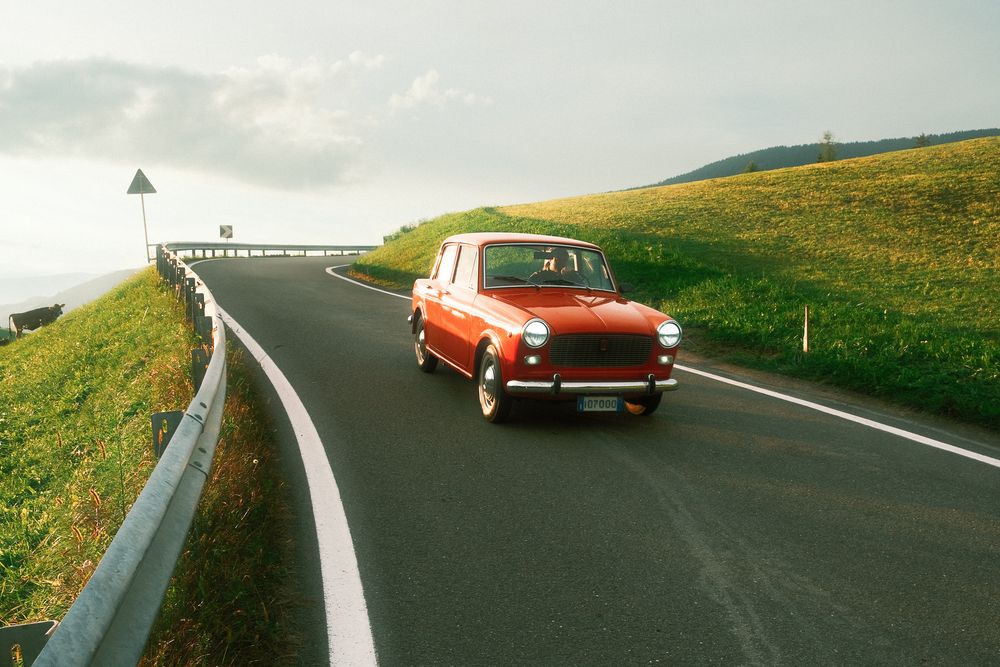 Vintage red car driving through curving mountain road in countryside