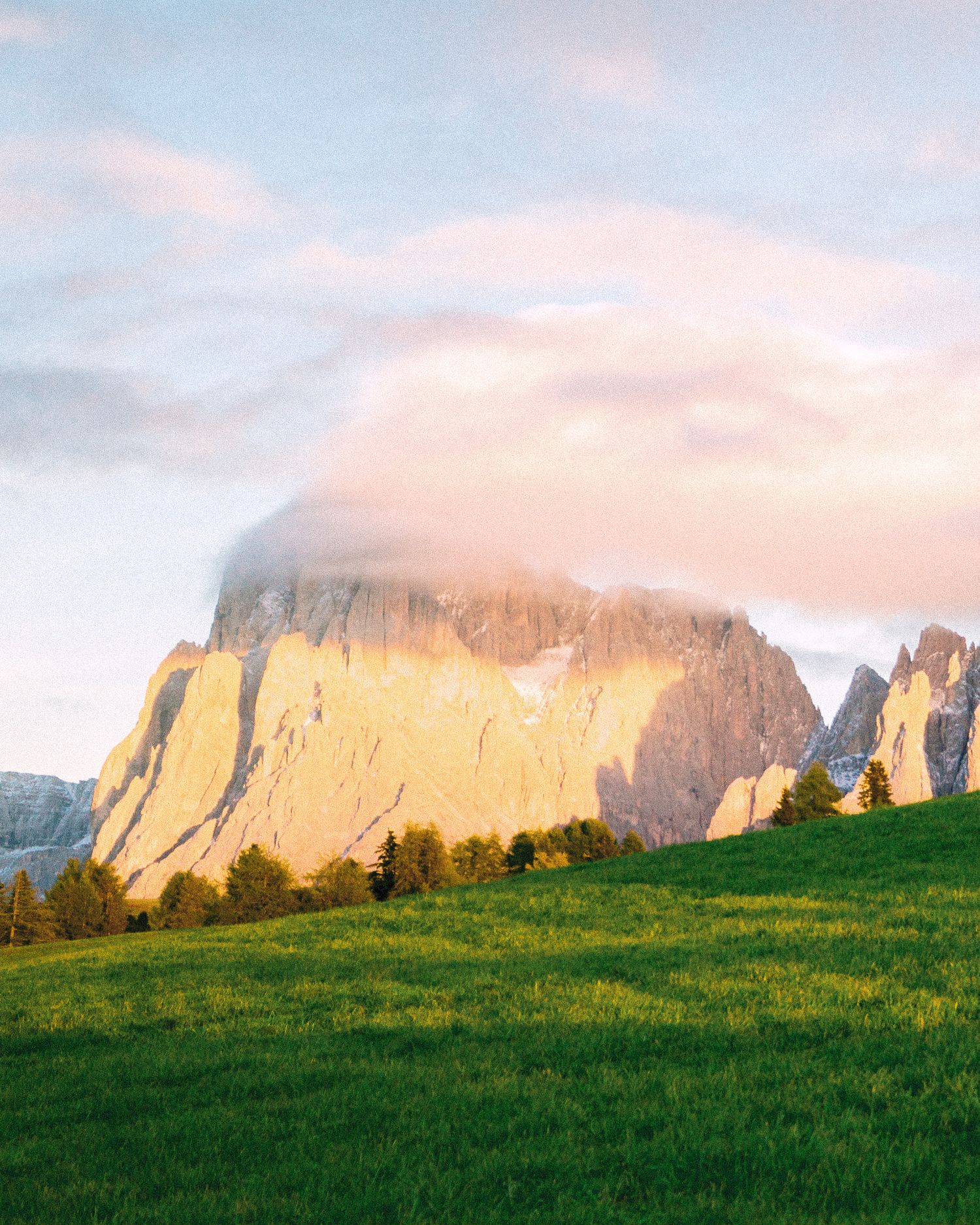 Sunset-lit mountain peak above a green meadow in the Dolomites.