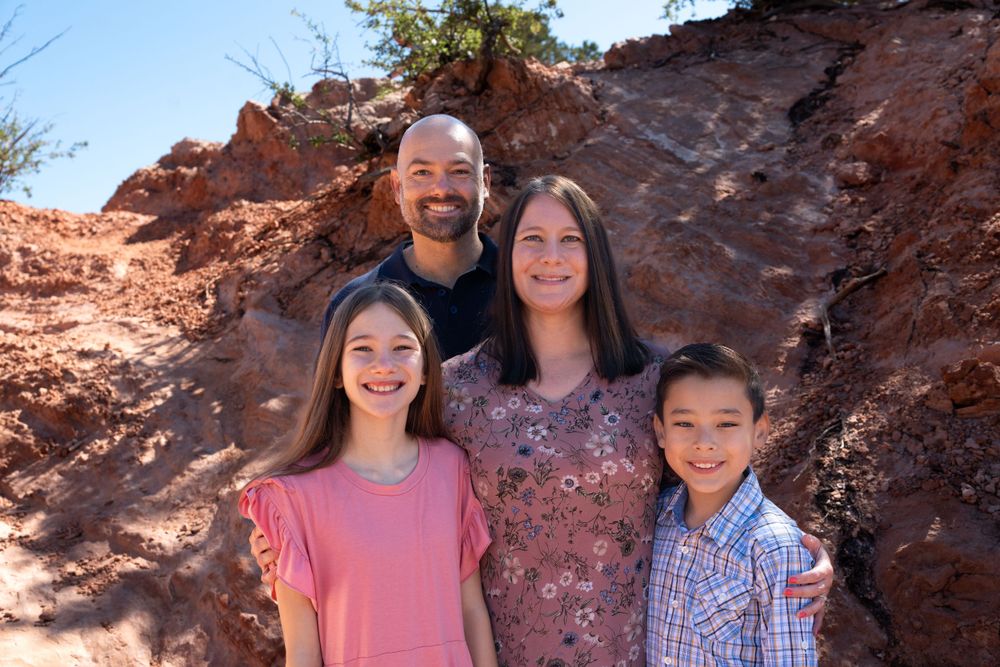 A happy family poses together against red rock formations on a sunny day.
