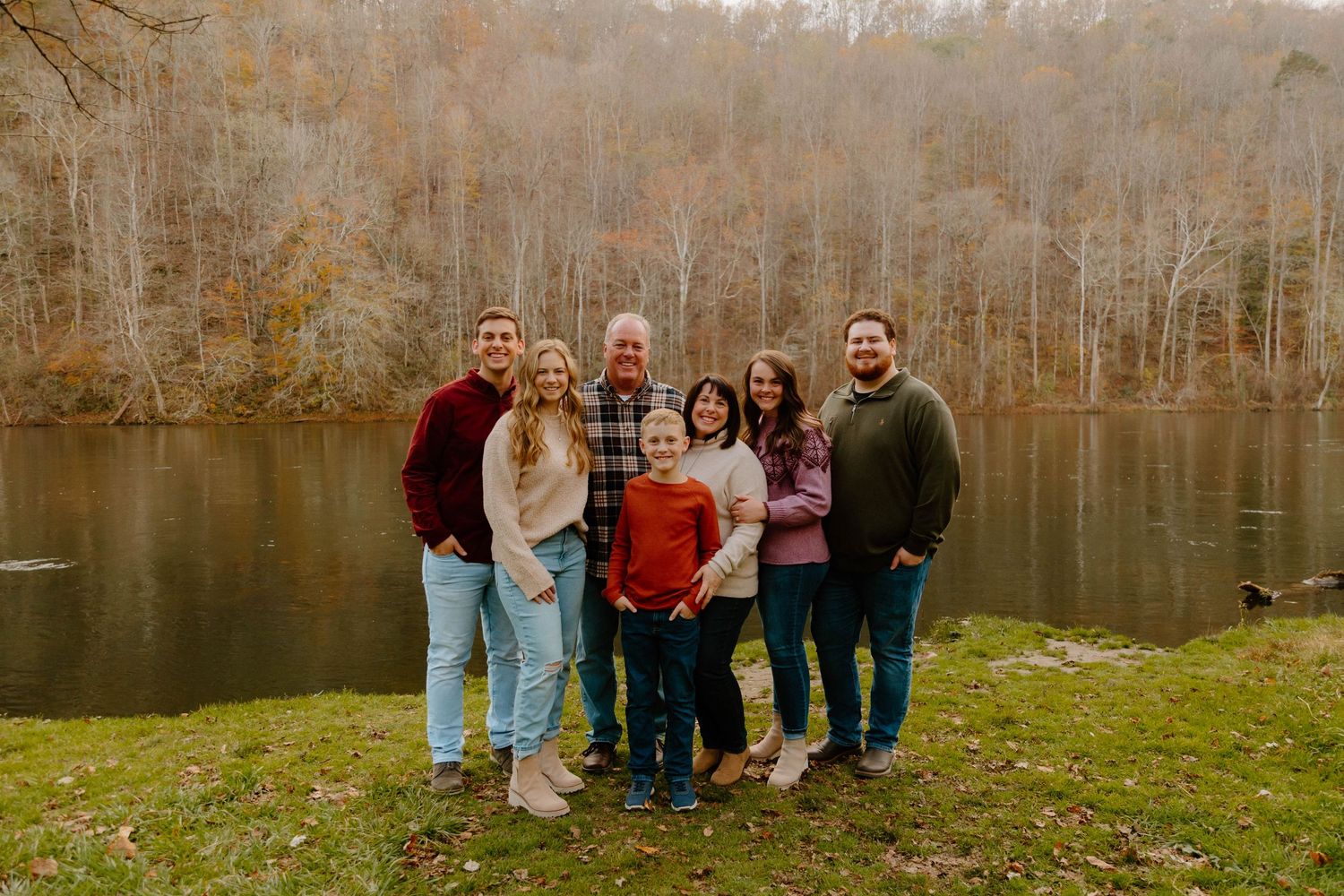 A family group poses together by a scenic lake surrounded by autumn trees.