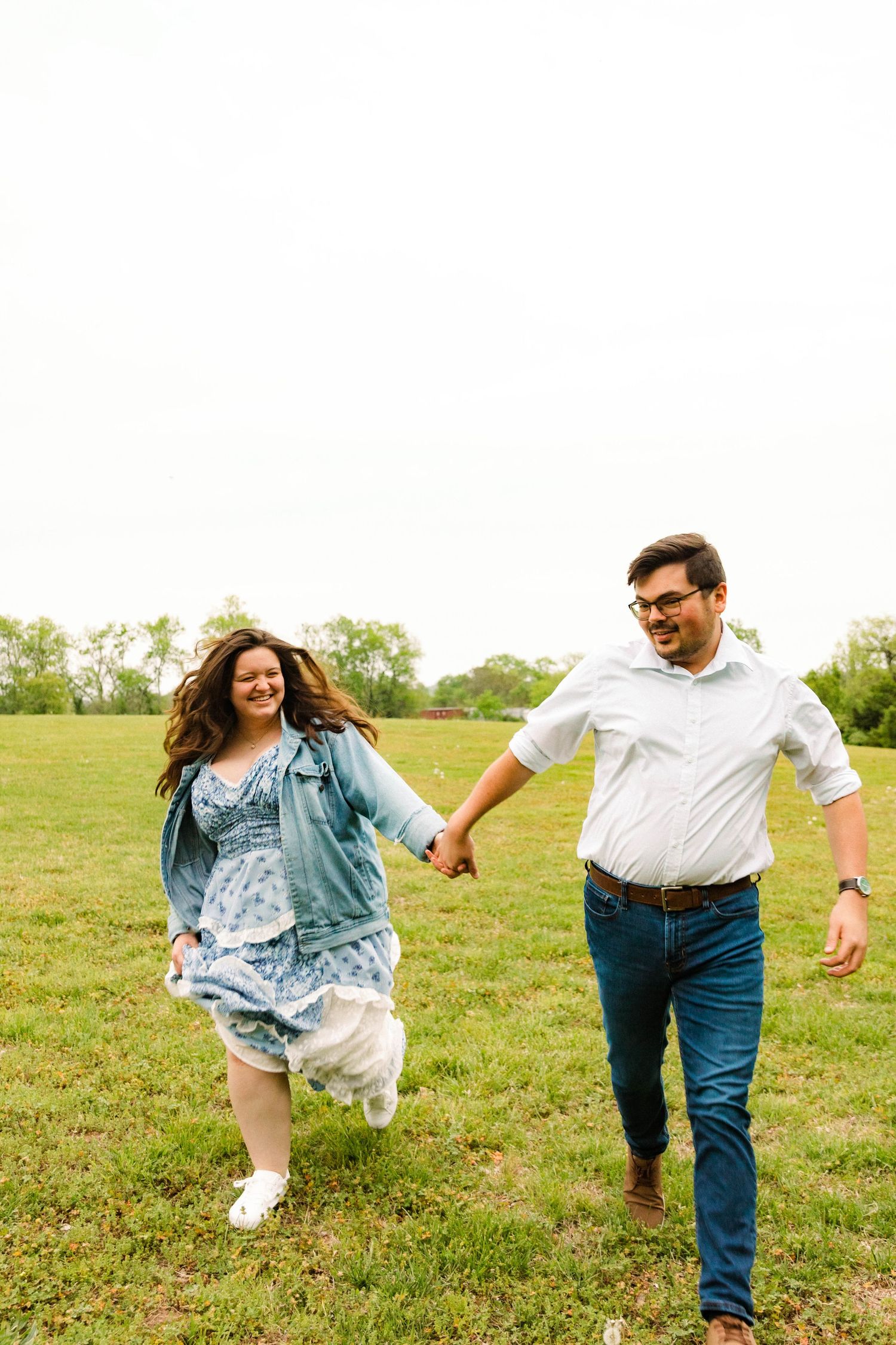 A joyful couple runs hand in hand through a grassy field on a sunny day.
