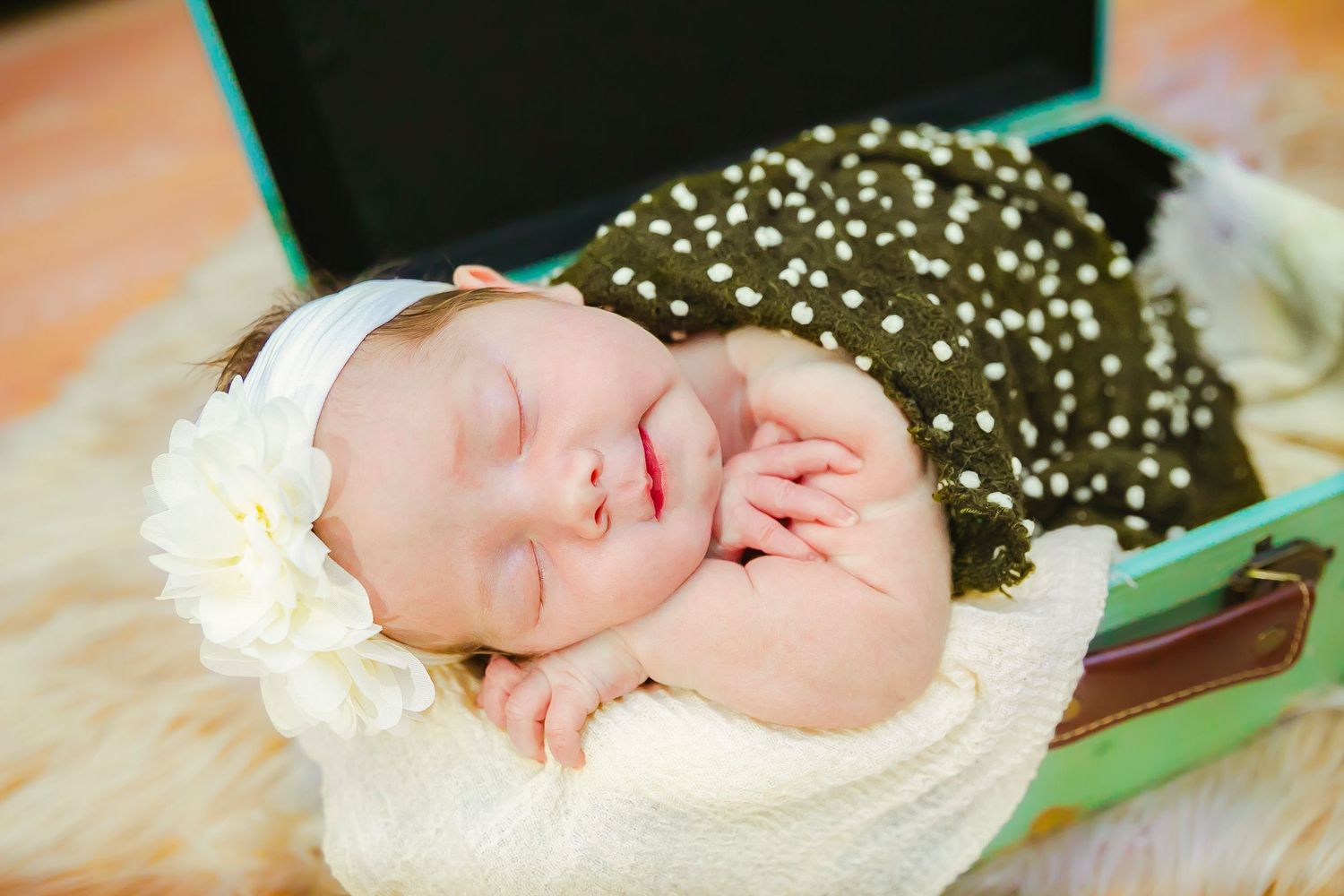 A sleeping newborn wearing a white headband lies peacefully on a soft blanket for her newborn photos.