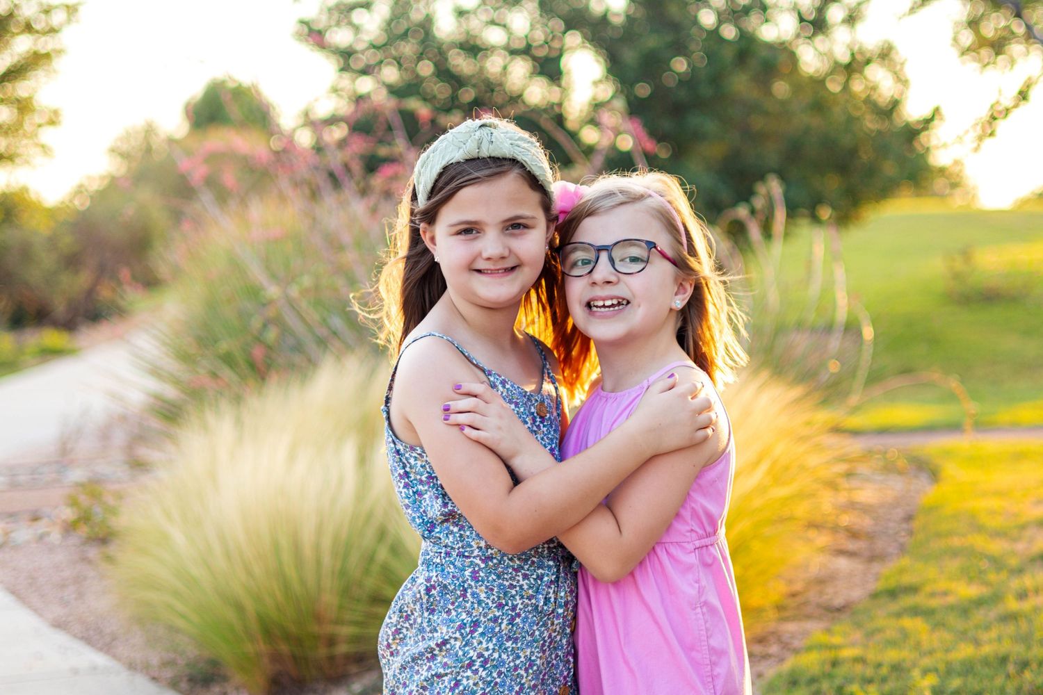 Two children hugging and smiling together on a nature path during golden hour sunset.