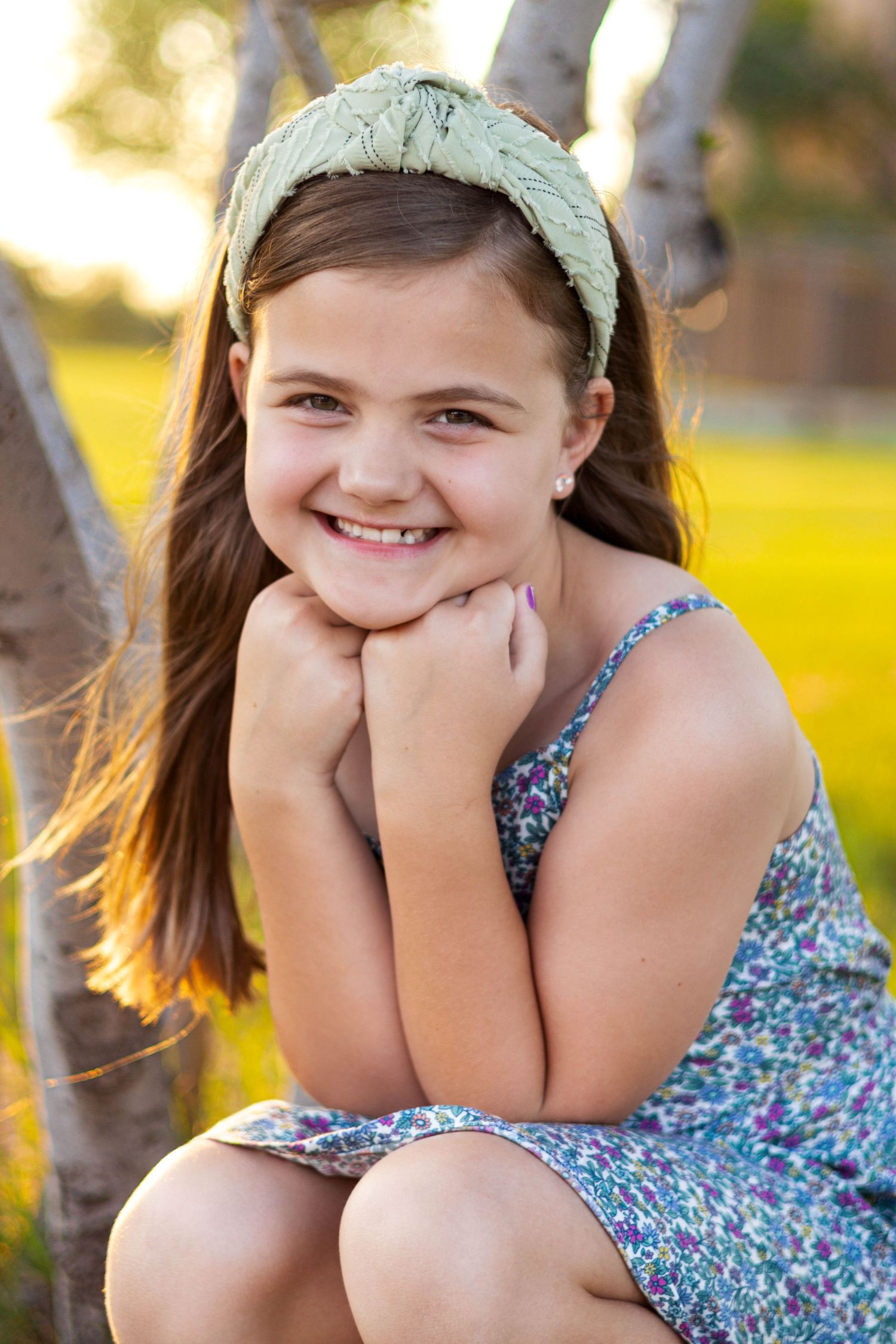 Outdoor portrait of a young child in a floral dress and mint headband posed casually on a sunny afternoon.