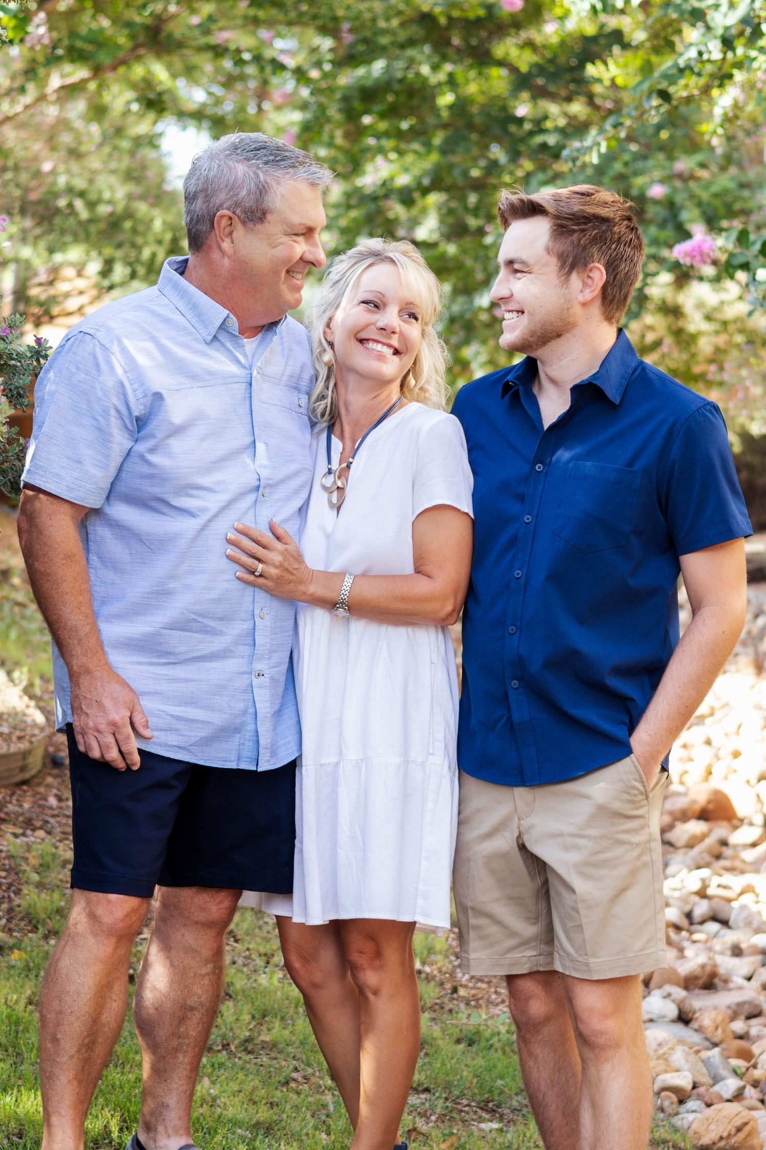 Three people in casual attire share a candid moment while laughing together outdoors on a sunny day.