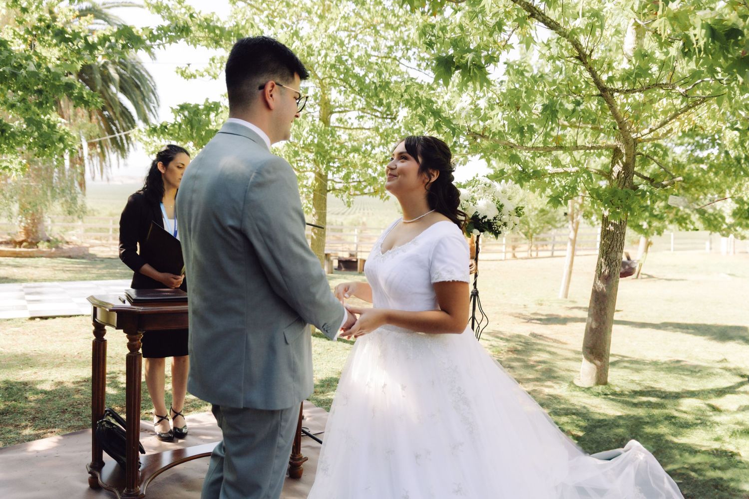 Bride and groom holding hands and exchanging vows at an outdoor garden wedding ceremony.