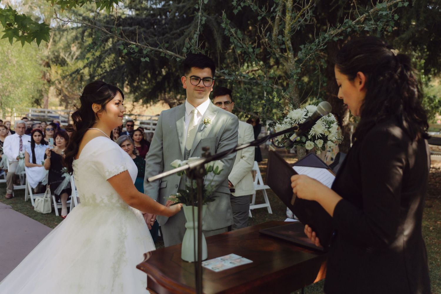 Bride and groom exchange vows at outdoor wedding ceremony with officiant at podium.