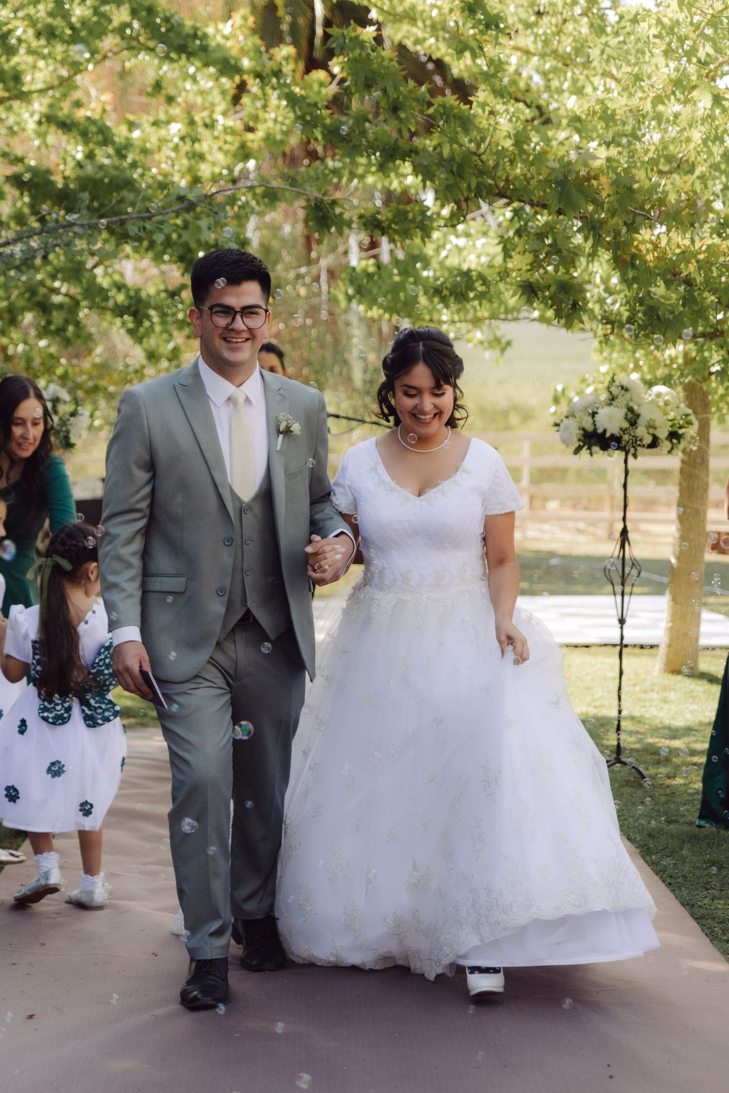 Smiling newlyweds walk hand in hand down the aisle after their outdoor wedding ceremony.