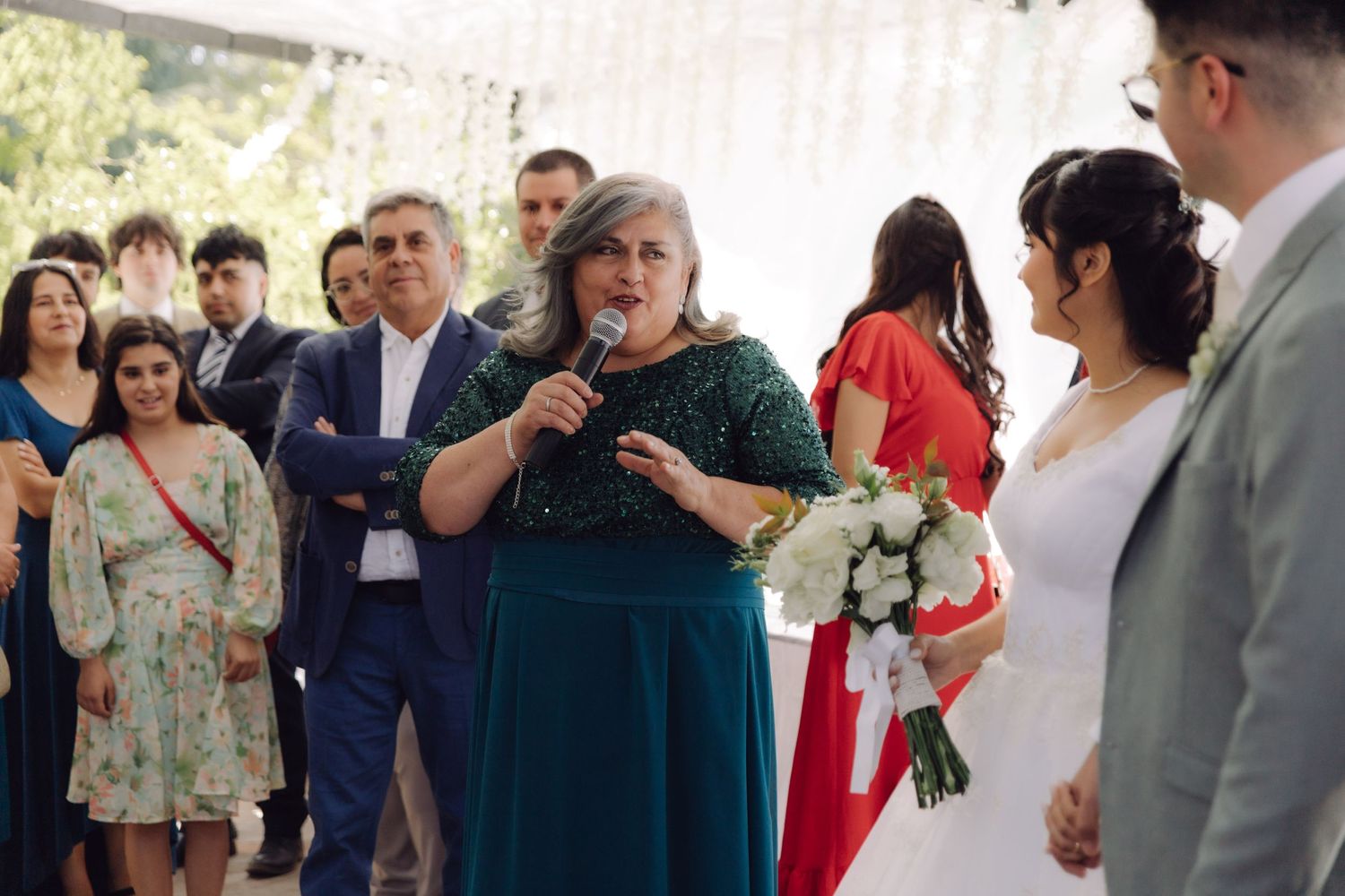 Woman in green dress gives speech with microphone at outdoor wedding reception.