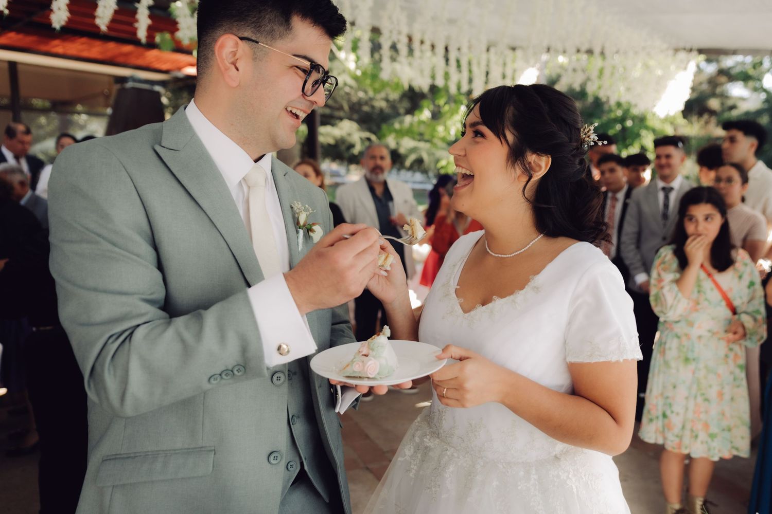 Newlyweds share a joyful moment feeding each other wedding cake at their outdoor reception.