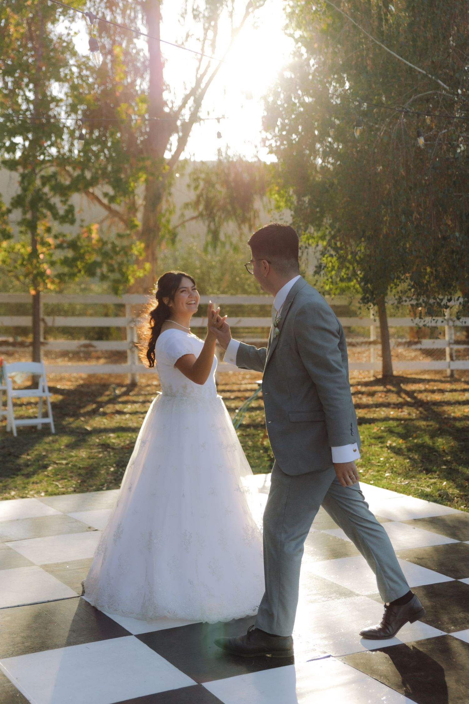 Newlyweds share their first dance on a checkered outdoor dance floor bathed in golden sunlight.