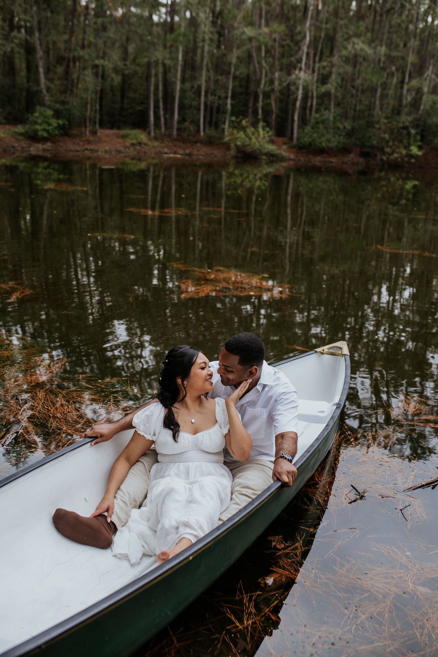 Romantic couple lounging in canoe on reflective lake surrounded by forest scenery.