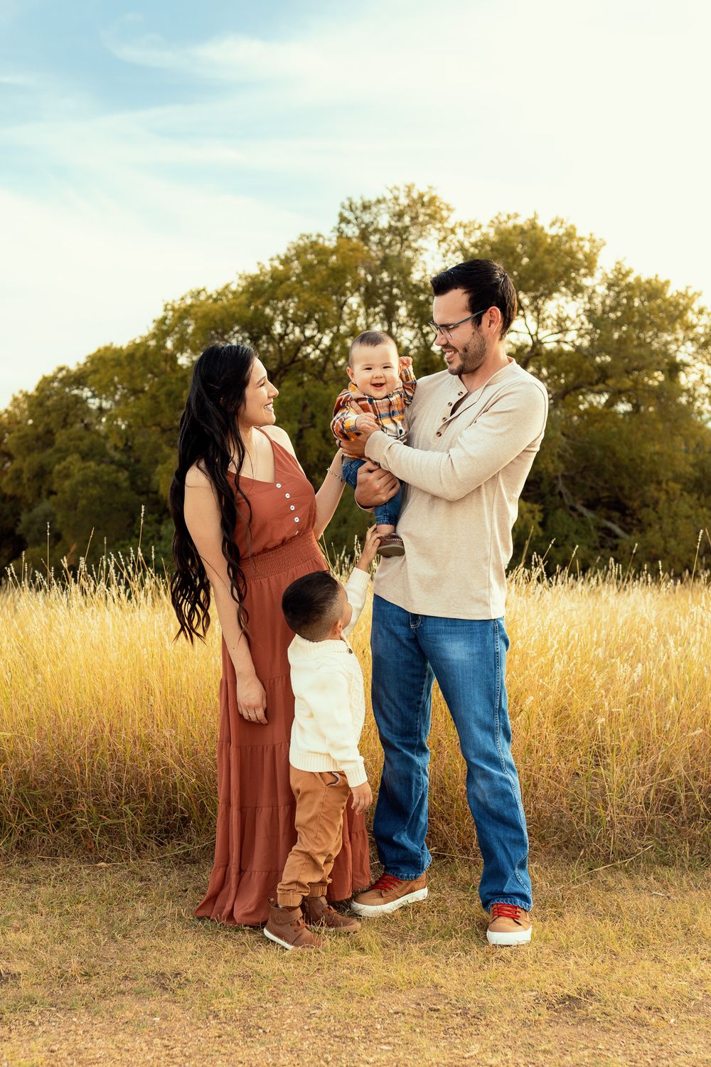 Family enjoying sunset together in tall golden grass field.