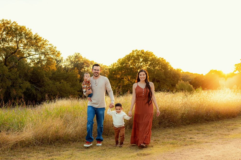 Family walking together through golden field at sunset.