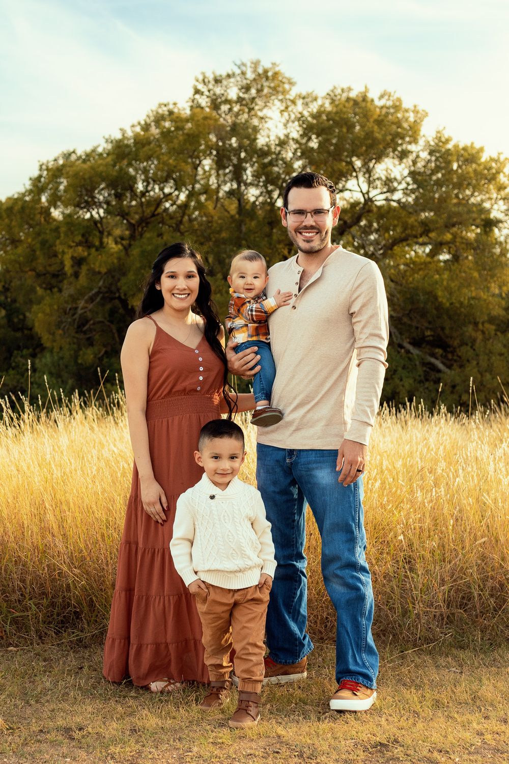 Family portrait with rust colored dress and cream sweater in golden field at sunset.