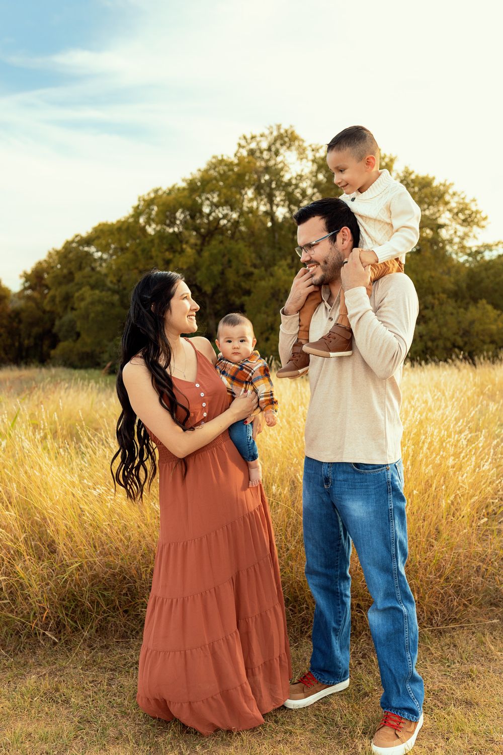 Parents holding children while playing in golden field at sunset.