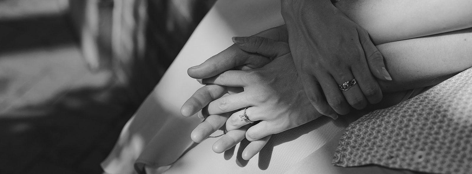 Two hands gently resting together in black and white, showing an intimate close-up moment.