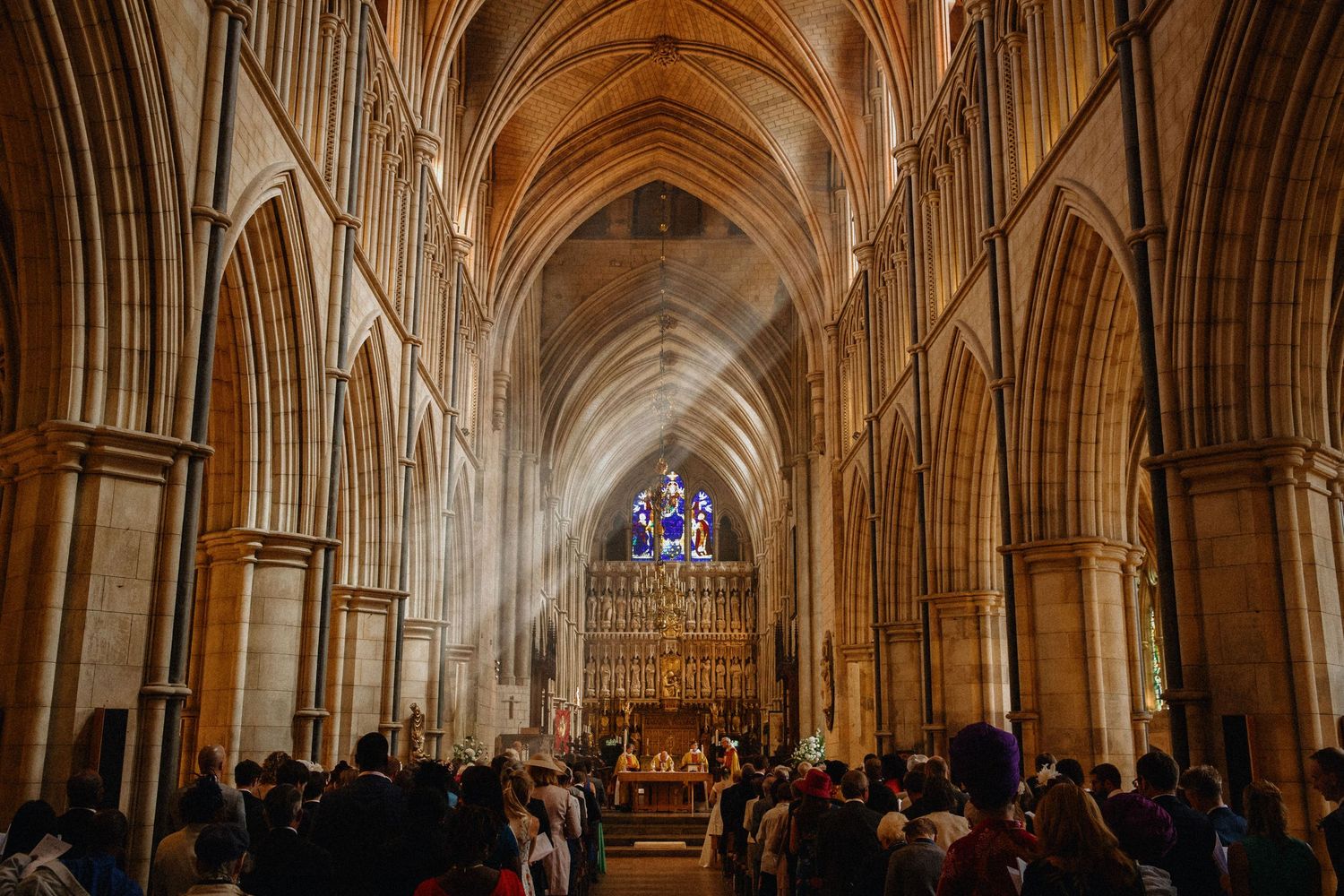 Sunlight pours into a Southwark cathedral with soaring ribbed vaulting and pointed arches. Wedding ceremony with guests seated