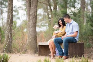 A couple sitting on a wooden bench in a pine forest with their small dog.