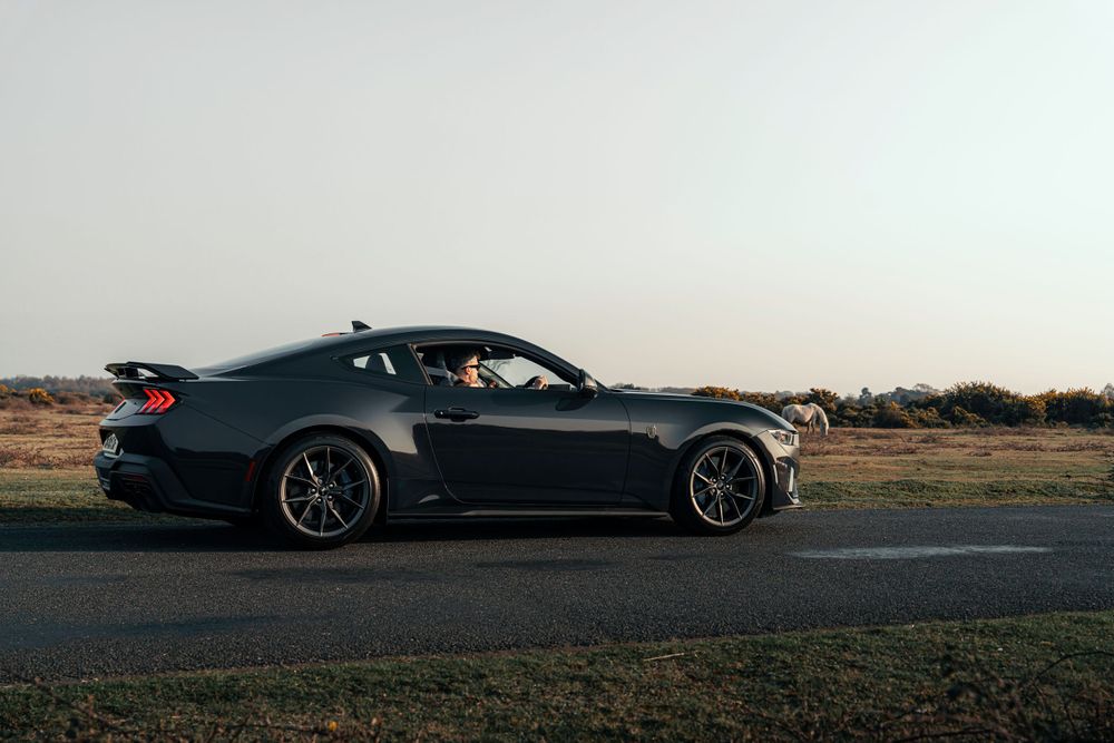 Profile view of a dark Mustang sports car on an empty road.