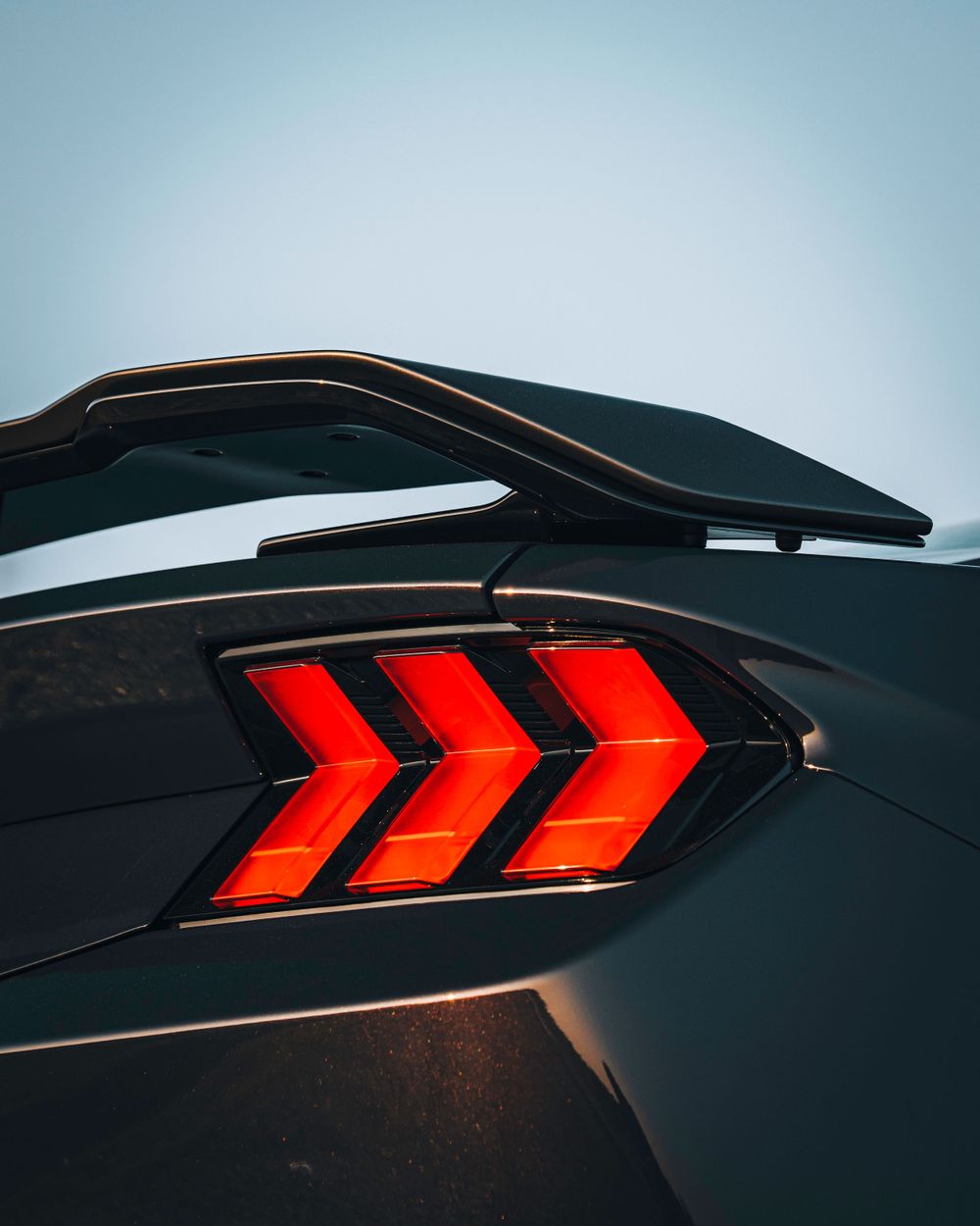Close-up detail of modern red arrow-shaped LED taillights on a black sports car.