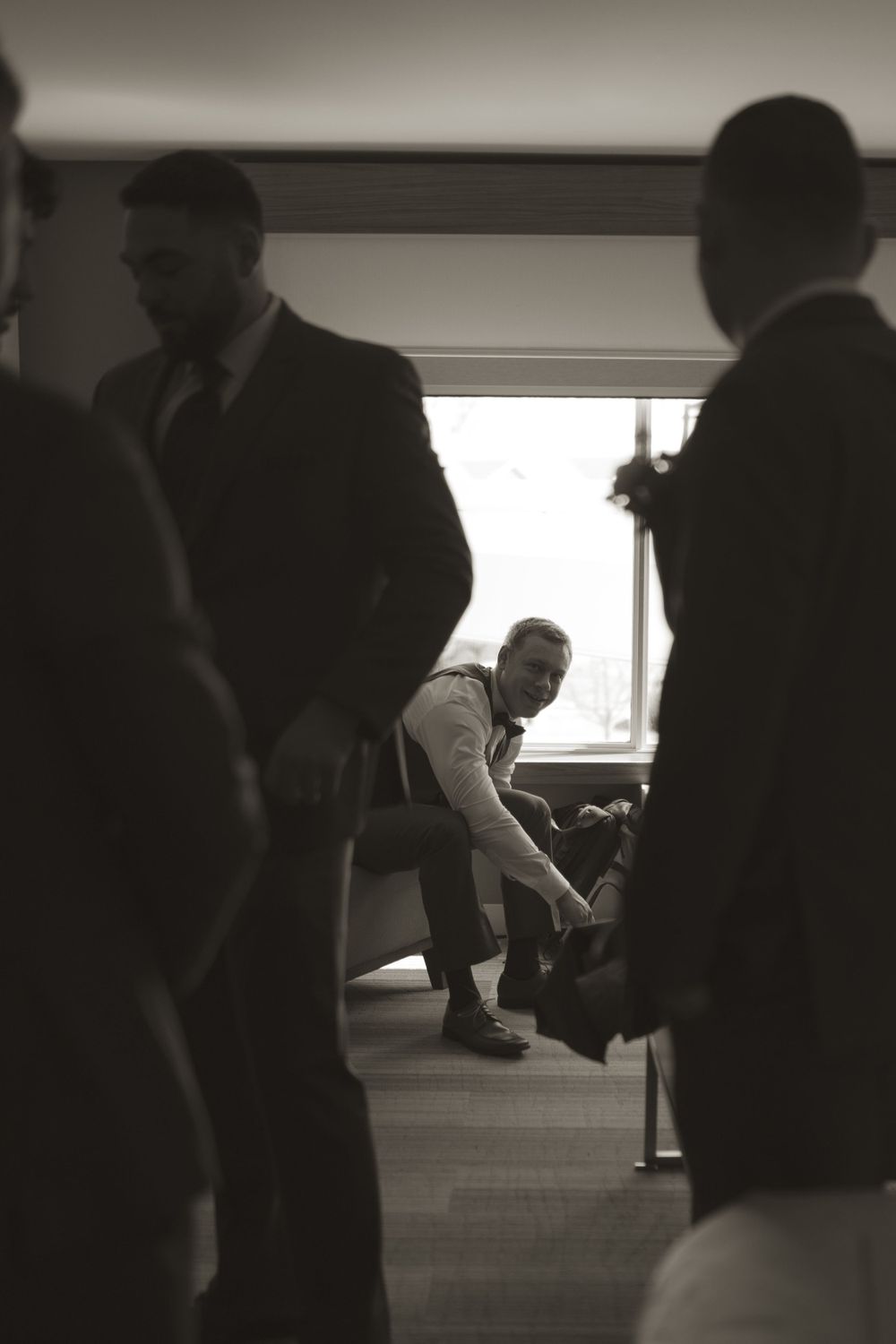 Silhouettes of groomsmen getting ready in a dimly lit room before a wedding ceremony.