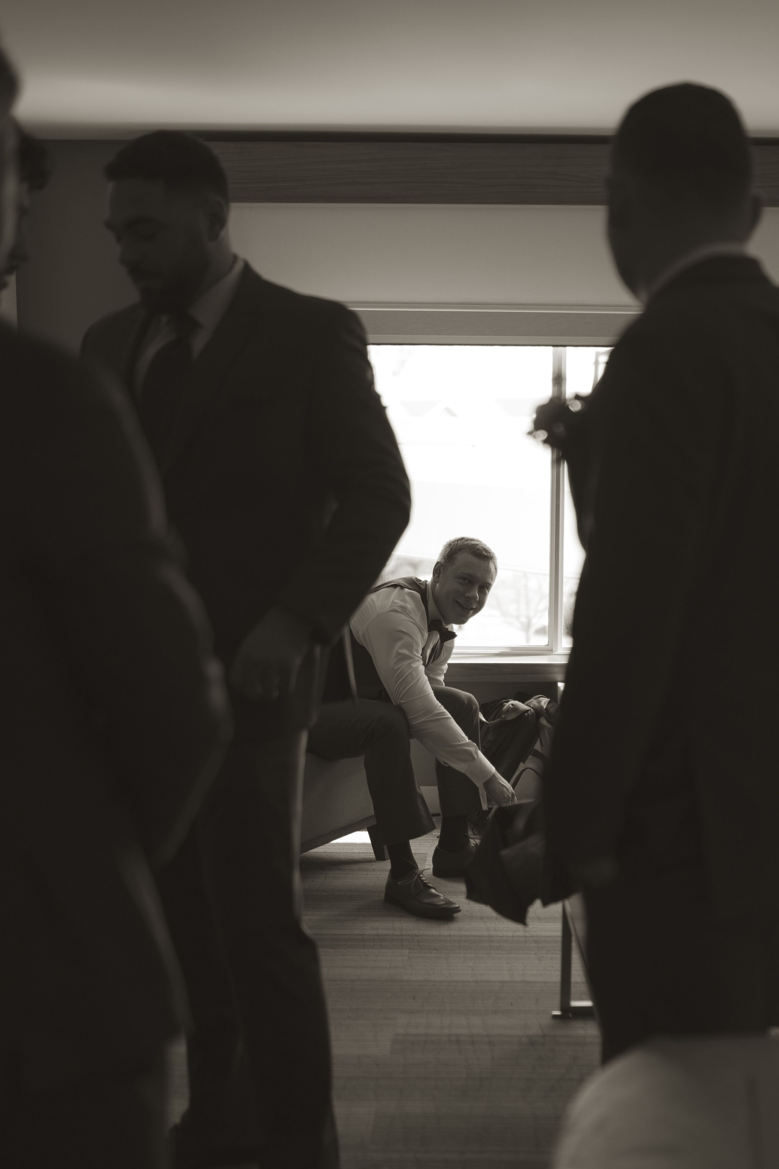 Silhouettes of groomsmen getting ready in a dimly lit room before a wedding ceremony.