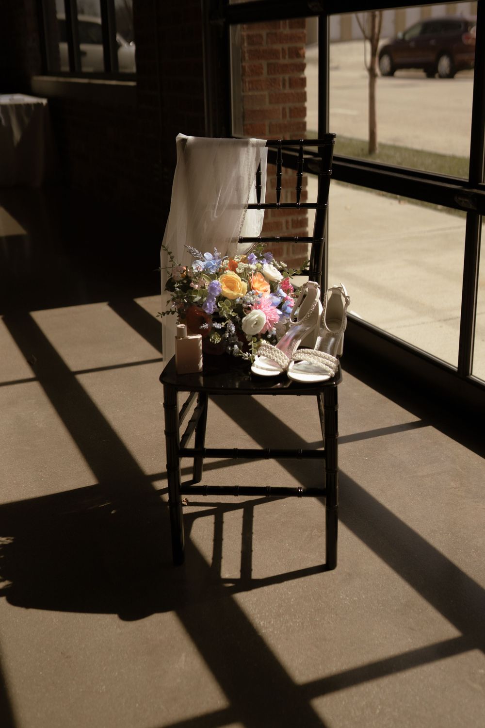 Dramatic shadows cast across floor with wedding bouquet on chair in sunlit room.